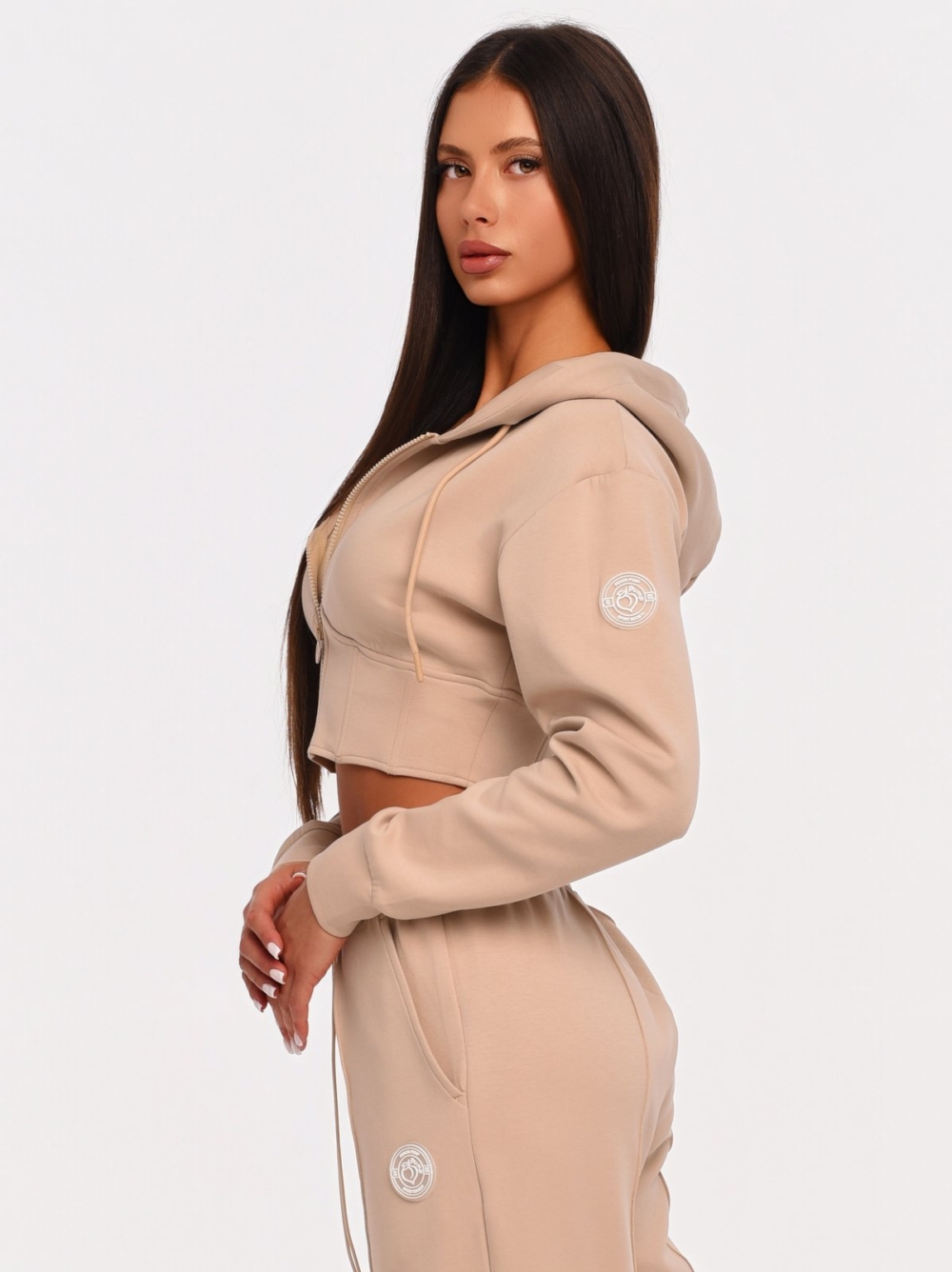 Beiger Cropped Hoodie mit gummiertem Peach Pump Logo auf der Schulter.